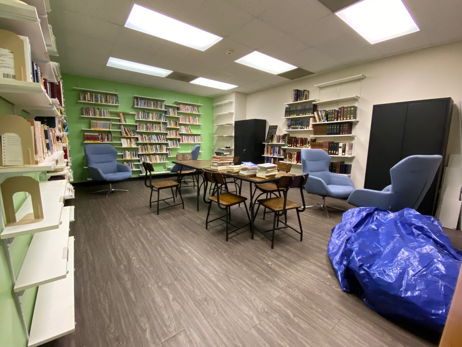 The library has several bookshelves of books, reading chairs, bean bags, and a table with chairs around it.
